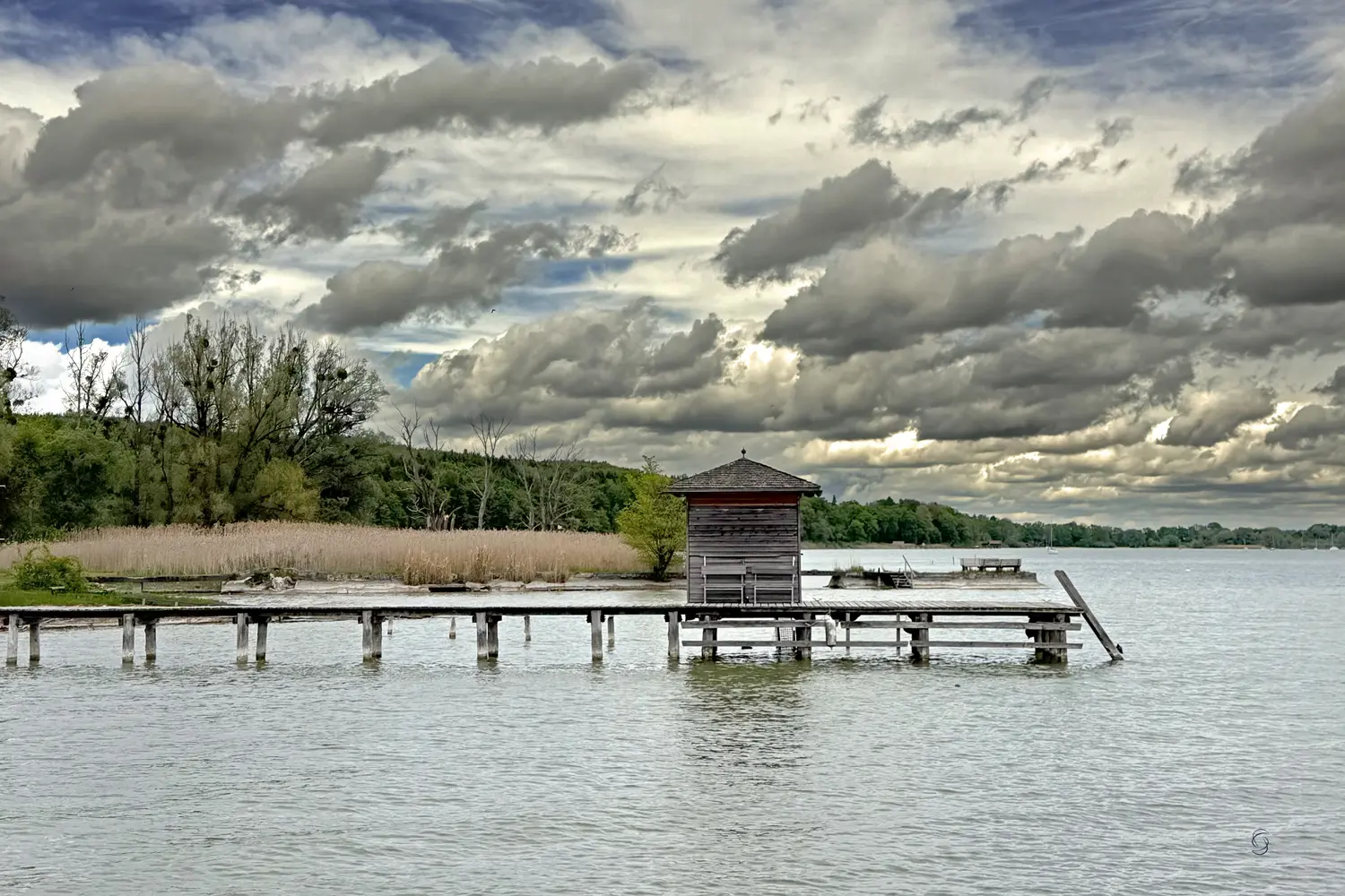 Einzeln abgesetzte Wolken über einem Bootssteg im Schilf am Ammersee. Windig-kalte Atmosphäre