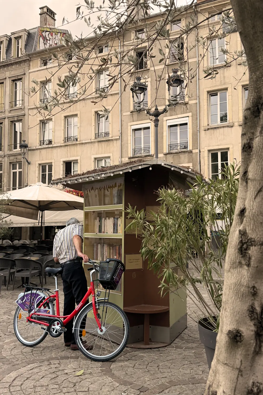 A man with a red bicycle is standing in front of a small book kiosk
