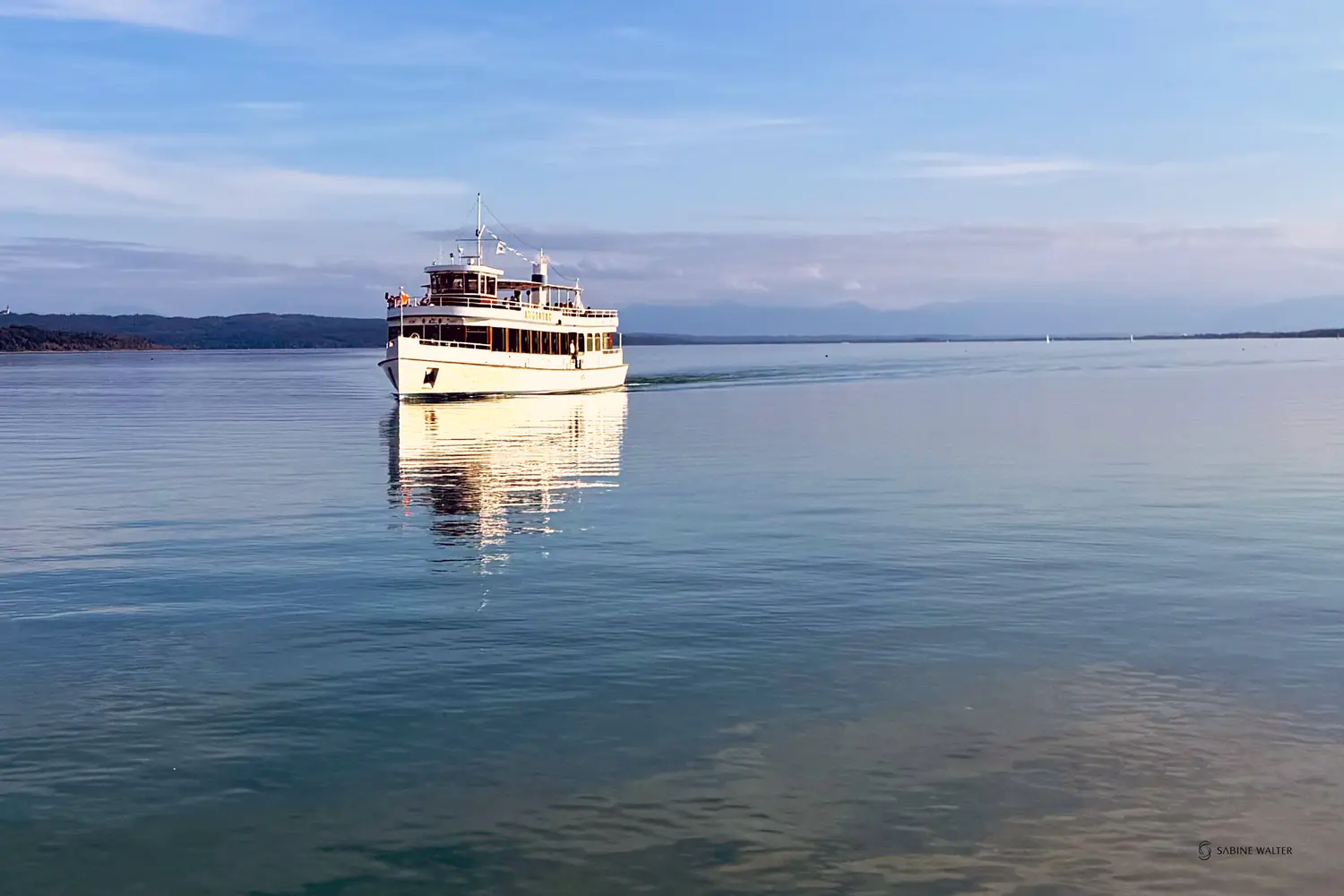 A steamboat glides across Lake Ammersee in the evening sun and heads towards the jetty.