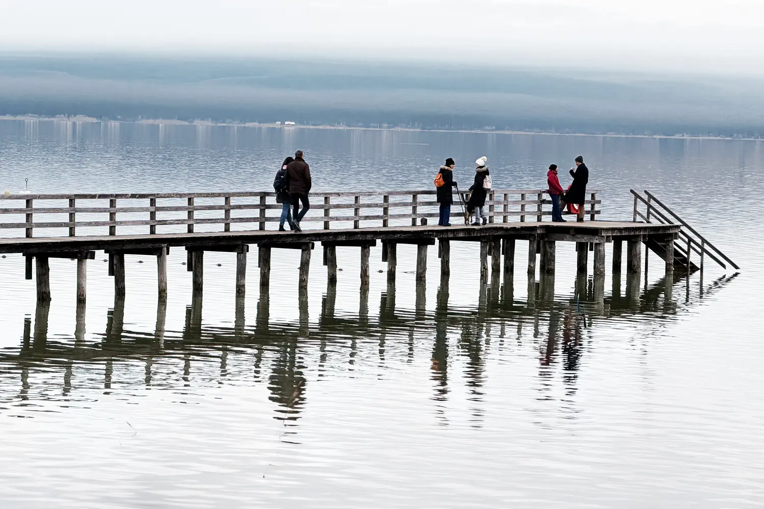 winterlich angezogene Menschen gehen und stehen auf dem Gemeindesteg in Schondorf am Ammersee